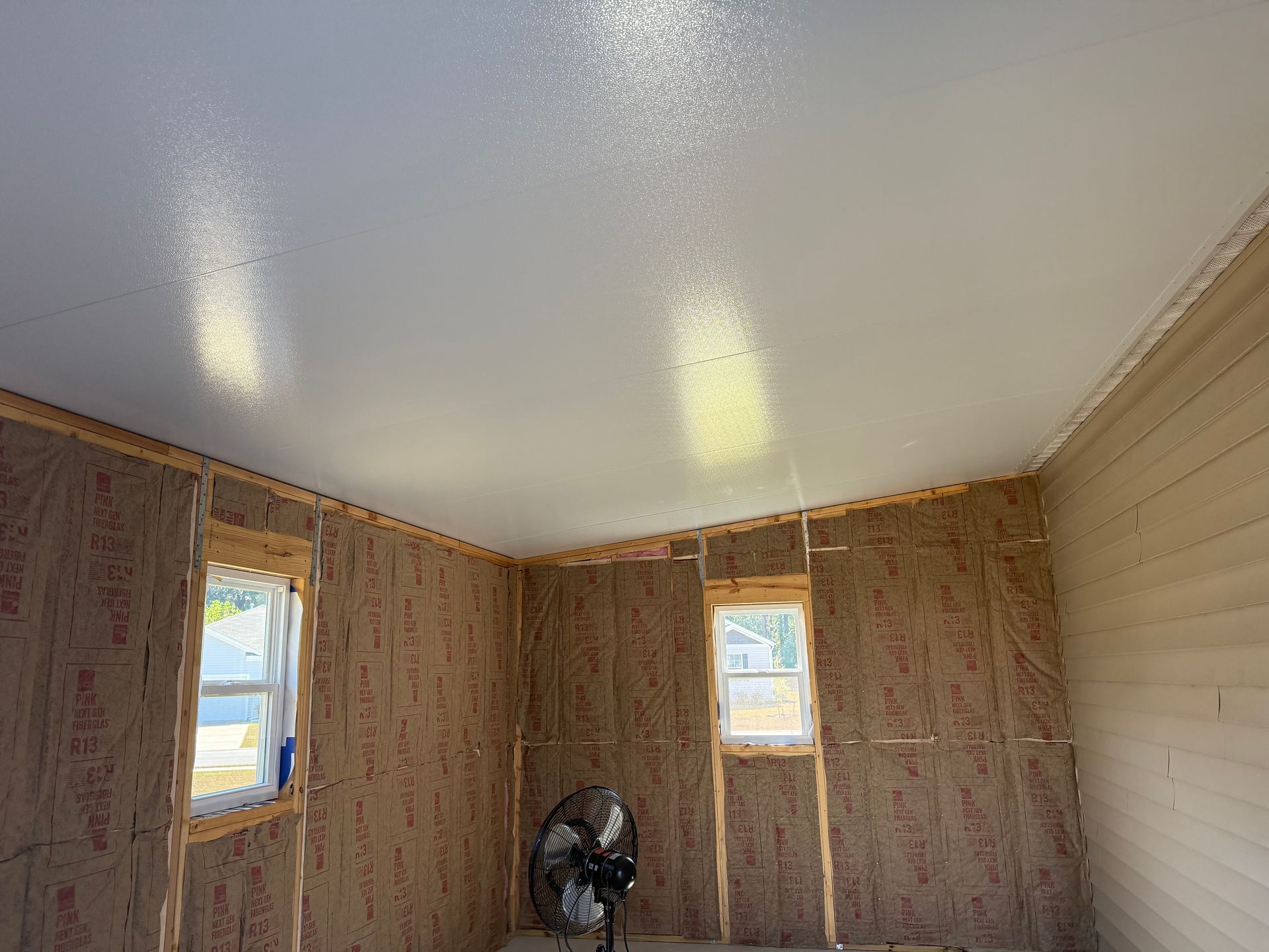 Interior view of a room under construction with insulated walls, windows, and a freshly painted ceiling.