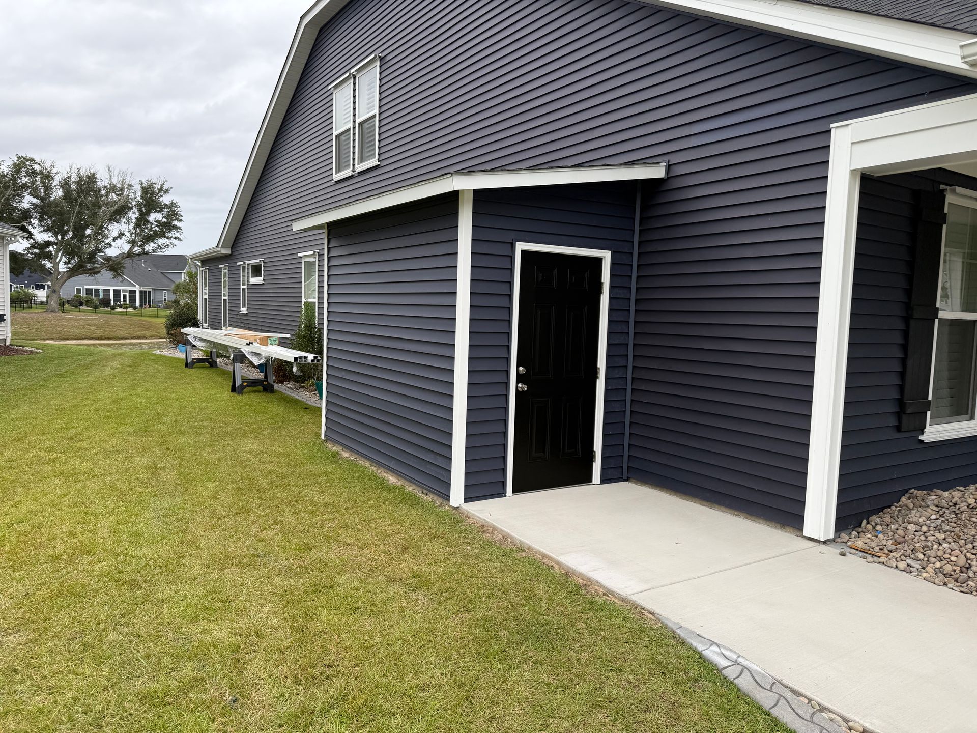 Dark blue house with white trim, small storage shed, and a concrete path.
