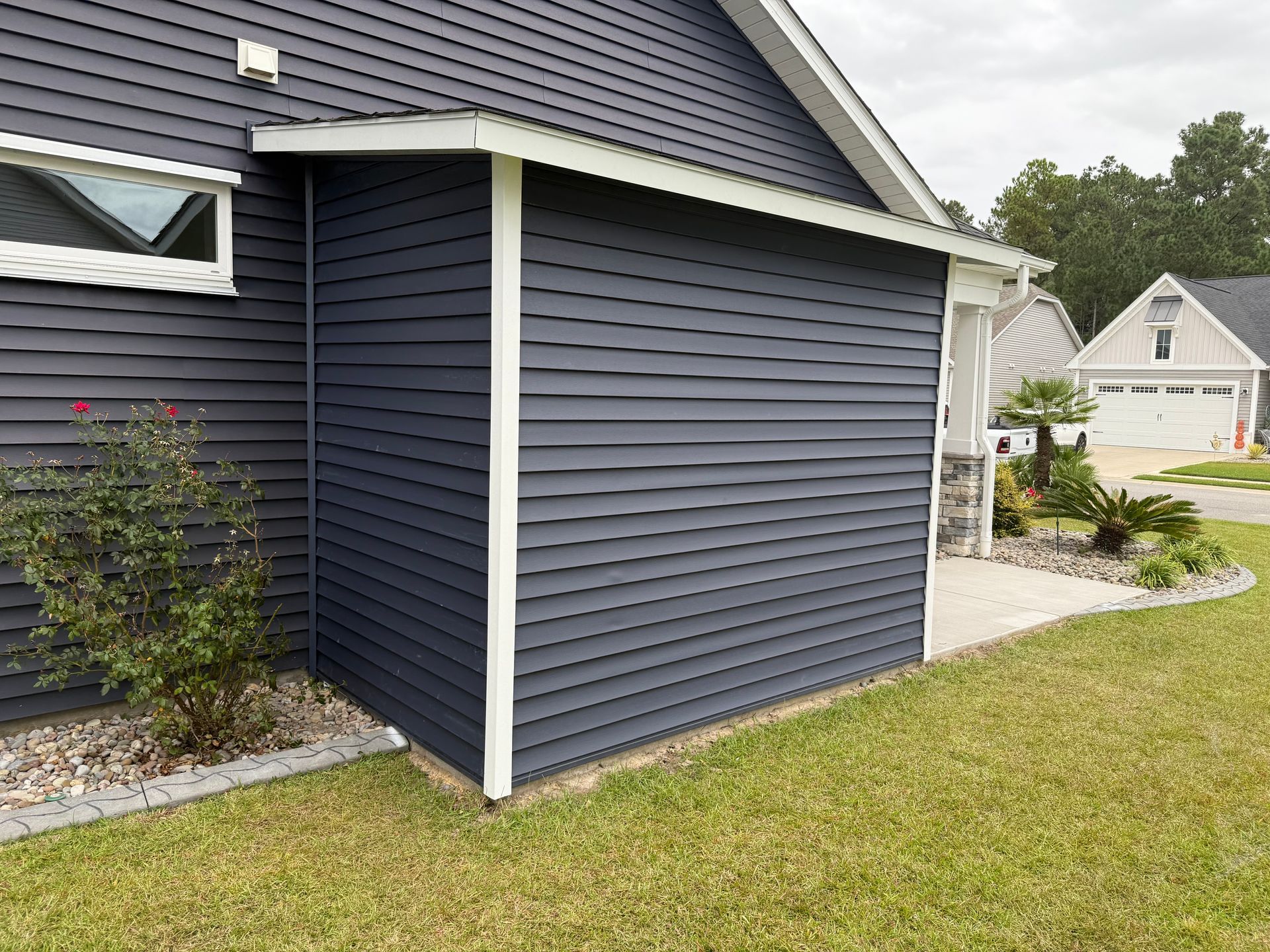 Dark blue siding on a house with white trim. A walkway and lawn are in the foreground.