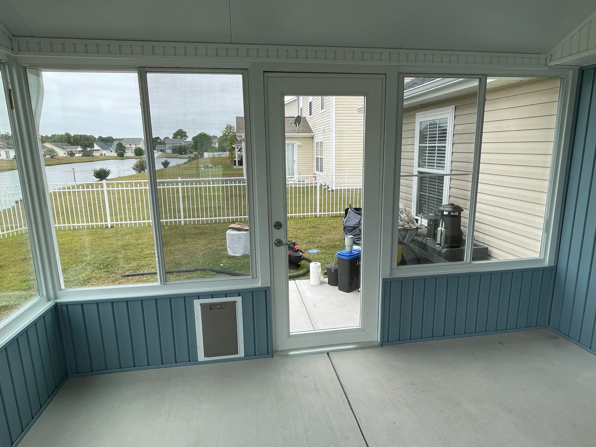 Enclosed porch with blue paneling, door, and windows overlooking a lake.