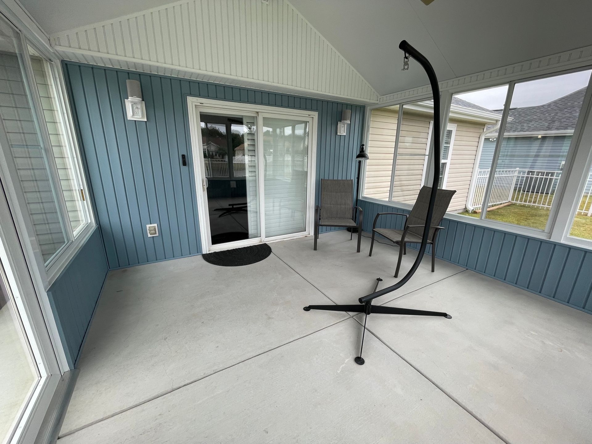 Sunroom with blue siding, sliding glass door, hanging chair, and outdoor chairs.