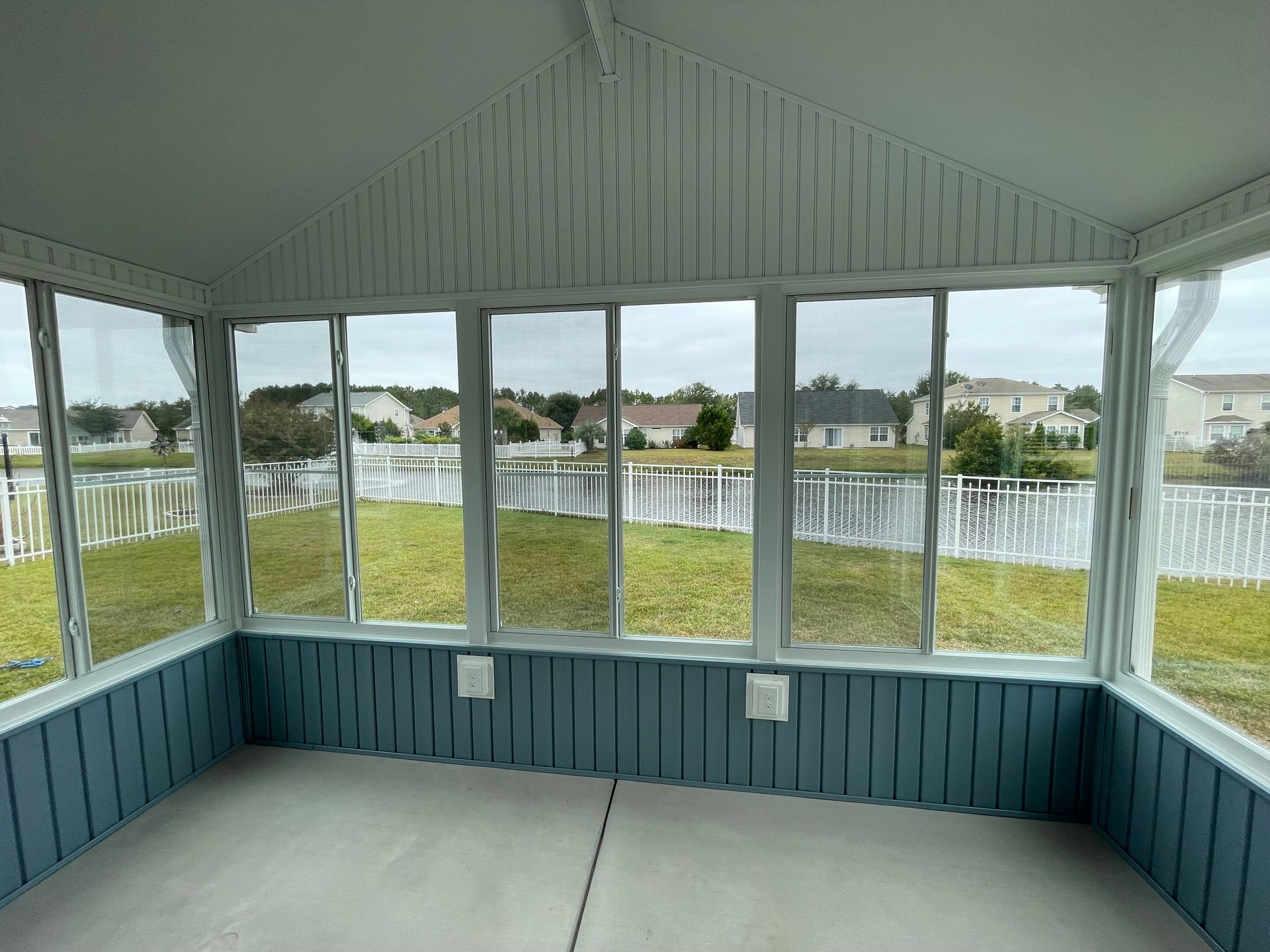 Enclosed porch overlooking a lake and houses, with blue paneling and white trim.