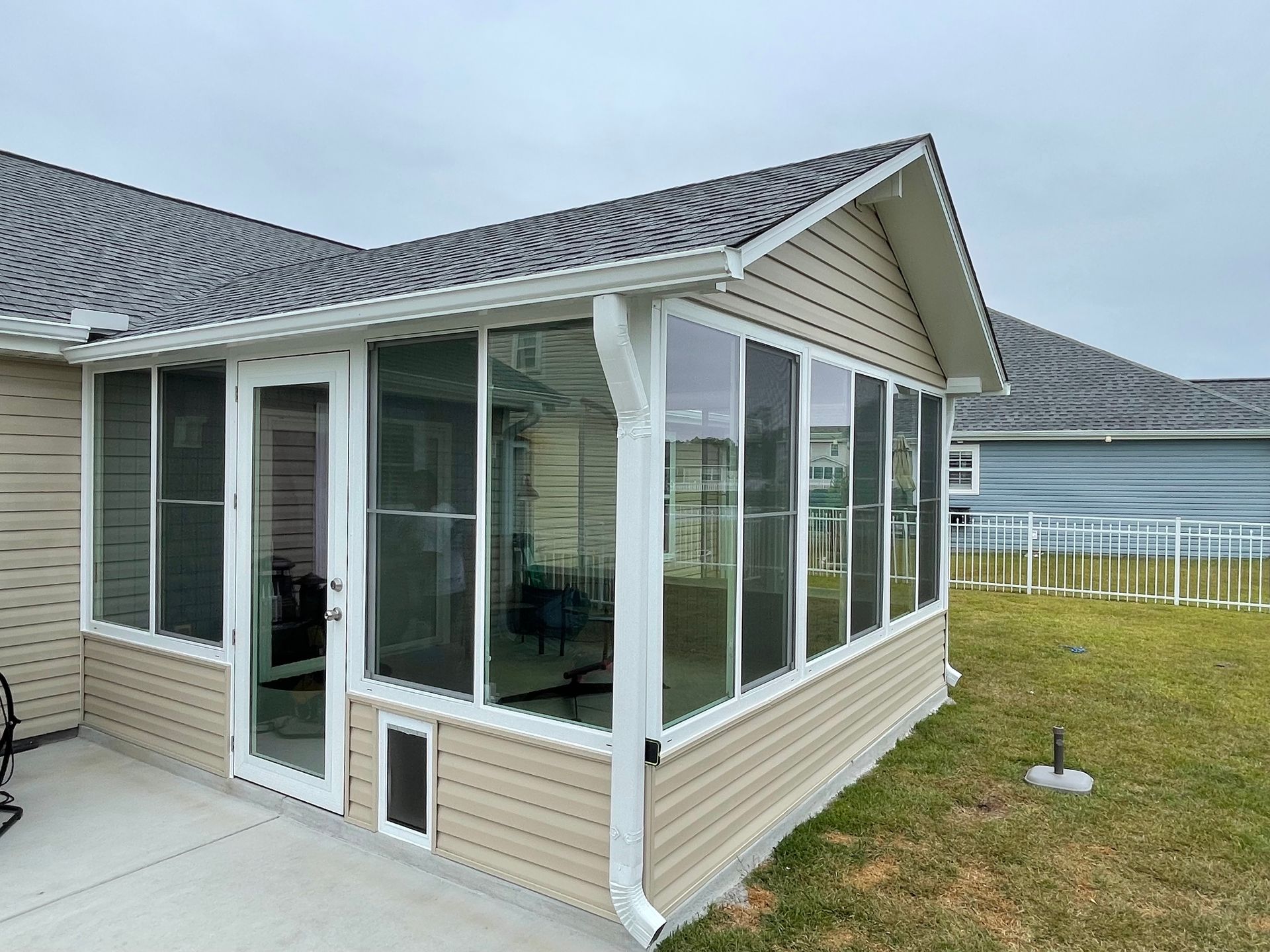 Sunroom addition with beige siding and screen windows, attached to a house with a gray roof.