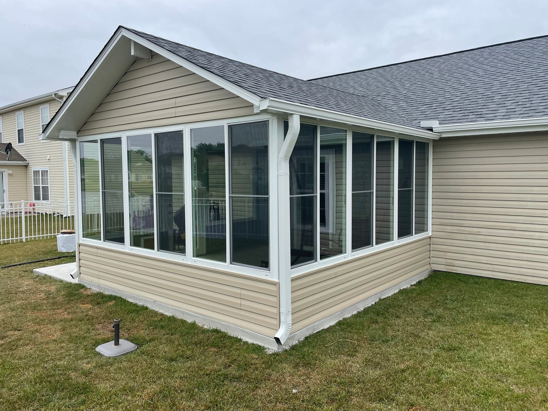 Screened-in porch attached to a house with beige siding and dark roof, set on a grassy lawn.