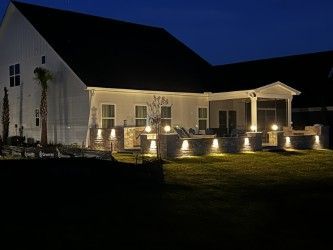 A white house exterior at night with outdoor lighting illuminating a patio and lawn.