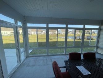Sunroom with white frames, glass windows overlooking a grassy yard, and a table with chairs.