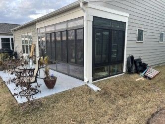 Screened-in porch attached to a light gray house, concrete patio, grass lawn.