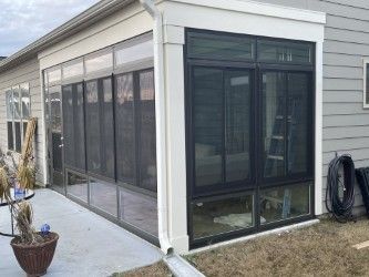 Sunroom addition with black framed windows and screens, attached to a light-colored house.