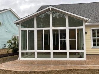 Screened-in porch attached to a house with white trim, overlooking a brick patio.