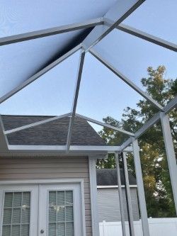 Screened-in patio with light blue roof, attached to a house with beige siding, overlooking a partially visible backyard and sky.