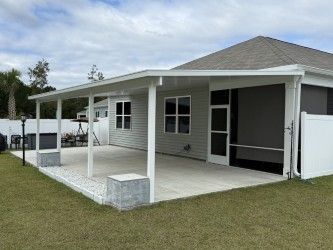 A covered patio attached to a light gray house. The patio has white columns and a concrete floor.