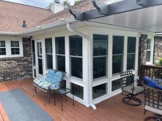 Screened-in porch on a wooden deck with seating. White frames, dark screens, and a brick house.