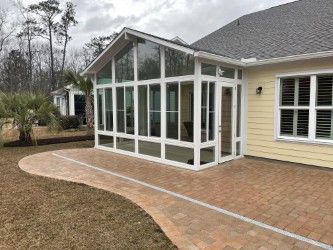 Sunroom addition with white frames, glass windows, brick patio, and yellow house exterior.