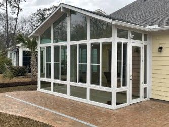 Sunroom with white frame, glass panels, and brick patio attached to a yellow house.