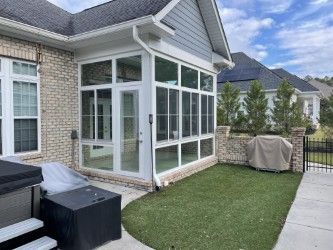 A sunroom with white frames and large windows on the side of a brick house with a small lawn.