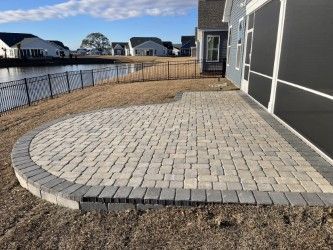 Brick patio with curved edge next to a house and a lake, set in a grassy yard.