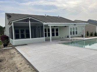 Backyard with a pool, patio, screened porch, and house. Concrete patio.