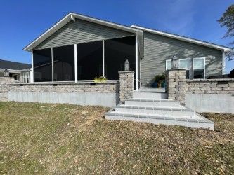 Gray house with screen porch, stone steps, and retaining wall against a blue sky.