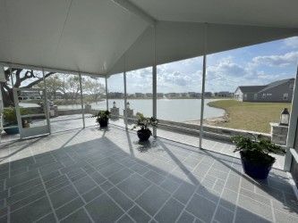 Sunroom with screened windows overlooking a lake, potted plants, and gray tiled floor.
