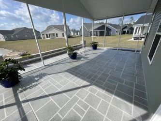 Screened-in porch with gray patterned floor, blue pots with plants, overlooking a suburban neighborhood on a sunny day.