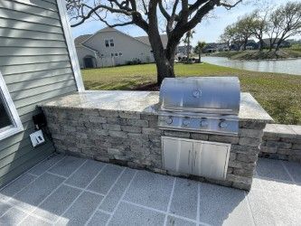 Outdoor grilling station with stainless steel grill, stone facade, and gray patio.