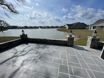 Patio overlooking a lake, with stone pillars and lanterns, under a cloudy sky.