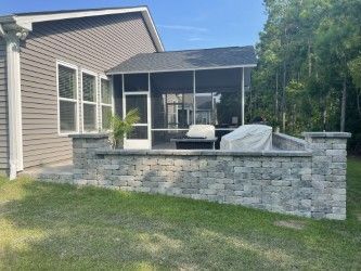 Screened patio with gray stone retaining wall, outdoor seating, and attached to a gray house.