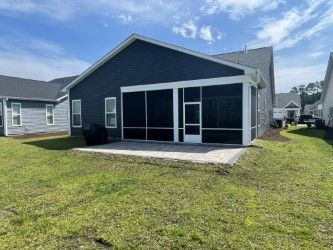 A blue house with a screened-in porch on a patio, viewed from a grassy backyard.