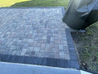 Brick patio with a dark border, next to grass. A black cover partially obscures the view.
