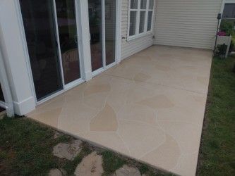 Beige concrete patio outside a house with sliding glass doors.
