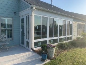 A sunroom with white frames and large windows attached to a light blue house, with a concrete patio.