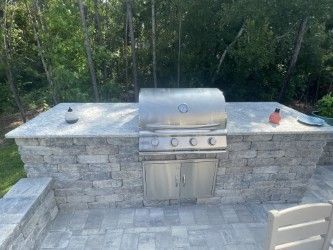 Outdoor kitchen with stainless steel grill, stone counter and cabinets.