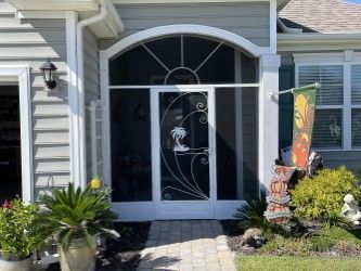 Screen door with white frame and decorative metal palm tree design; arched top, entryway.