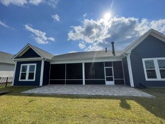 Blue house with screen porch and paver patio, set against a sunny, blue sky.