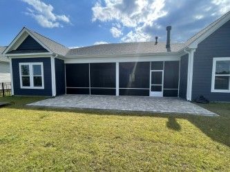 Blue house with screened porch and gray patio on a green lawn under a partly cloudy sky.