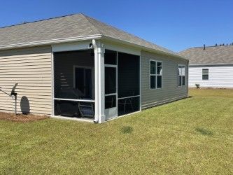 A screened-in porch attached to a light-colored house with a grassy yard and clear blue sky.
