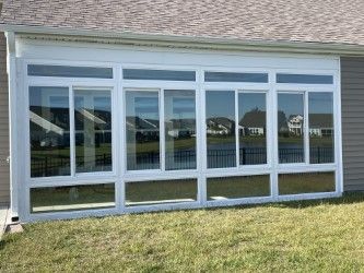 White framed sunroom with large windows, set against a house and grass lawn.