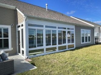 Sunroom addition with white frames, many windows, gray siding, and a grassy backyard.