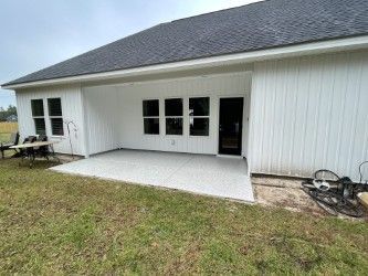 Backyard patio with white siding and dark roof, overlooking a grassy area.