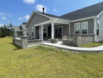Gray house with a concrete patio and low walls, a sunny lawn, and a blue sky.