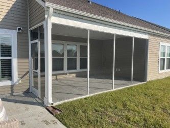 Screened-in porch attached to a beige house, with concrete floor and white framing.