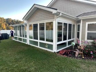 A white screened-in porch attached to a beige house, next to green grass.