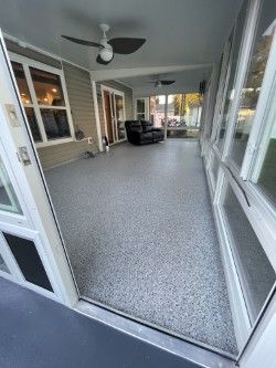 Enclosed porch with grey flecked floor, windows, ceiling fans, and furniture.