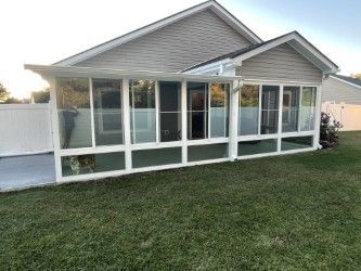 Screened porch with white frame, attached to a house with beige siding, overlooking a green lawn.