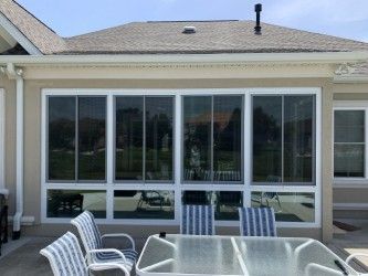Patio with large windows, white frames, outdoor seating. Beige exterior, grey roof.