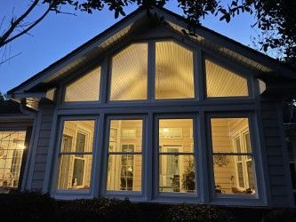 Exterior view of a house at dusk, lit from within, with large windows reflecting warm light.