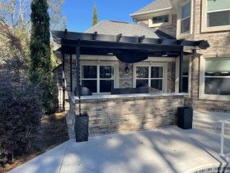 A patio with a stone wall, black pergola, and outdoor seating next to a brick building.