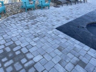 Gray brick patio surrounds a dark pool; turquoise chairs in background.
