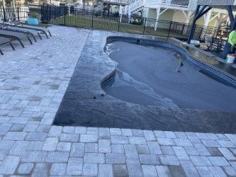 Pool with dark trim, light pavers, and lounge chairs in an outdoor setting.