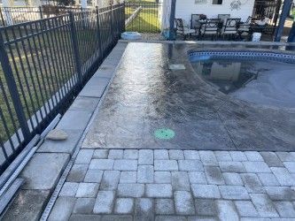 Concrete patio with pool, fence, and stone pavers in an outdoor setting.